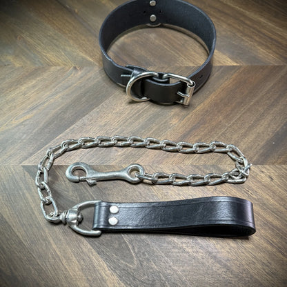 Hero-tilt view of a handcrafted 1.75" black leather collar with nickel-plated steel hardware and an attached heavy chain leash.