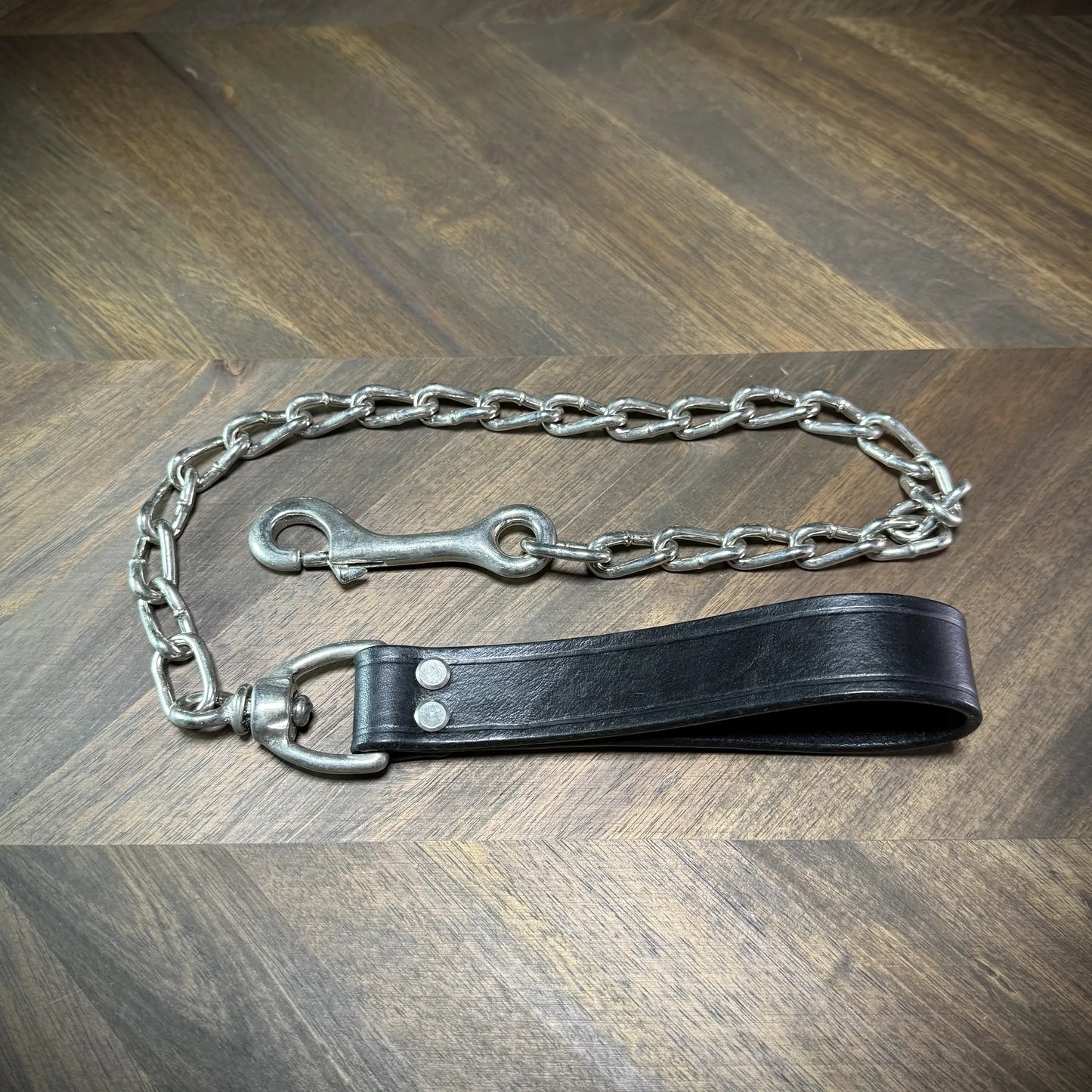 Front-facing view of a black leather loop tether with polished nickel-plated steel hardware, double rivets, and a structured chain assembly.