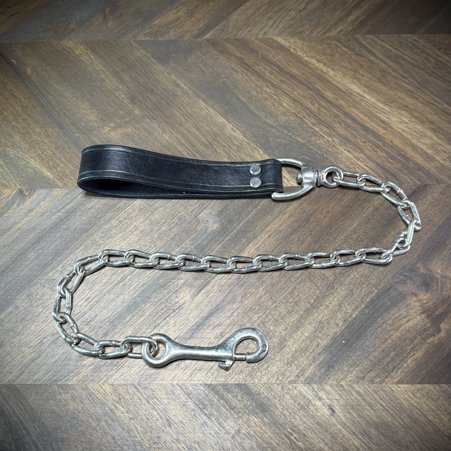 Hero-tilt view of a handcrafted black leather loop tether featuring nickel-plated steel rivets, a swiveling panic snap, and a classic link chain.