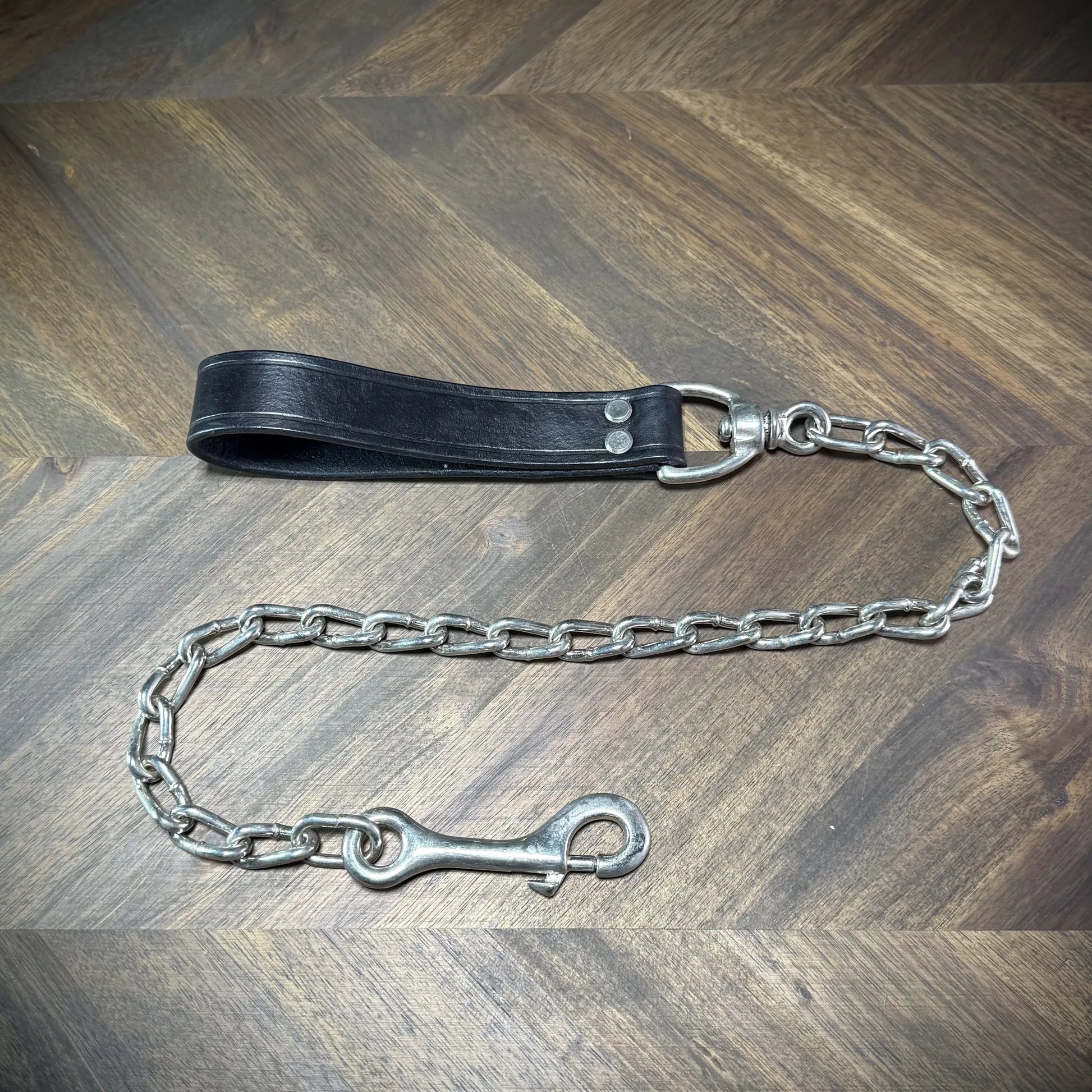 Hero-tilt view of a handcrafted black leather loop tether featuring nickel-plated steel rivets, a swiveling panic snap, and a classic link chain.