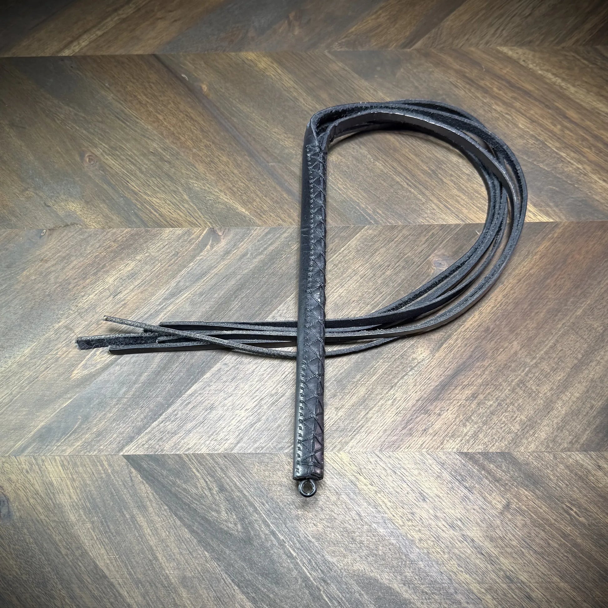 Studio-craft view of a Knotty Oso impact martinet handcrafted from black leather, featuring a hand-wrapped handle and multiple heavy straps.
