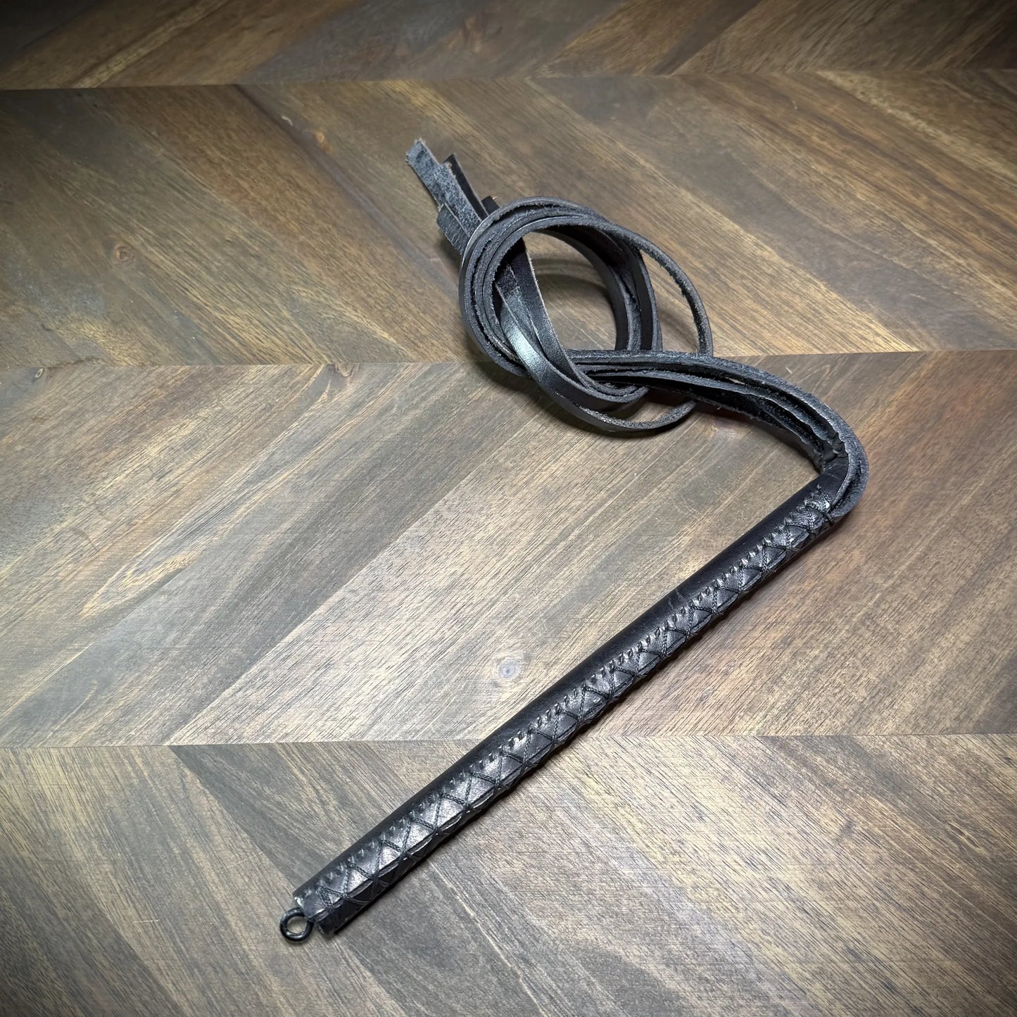 Hero-tilt view of a coiled black leather impact martinet with heavy-weight straps, showcasing structural material flexibility and construction density.