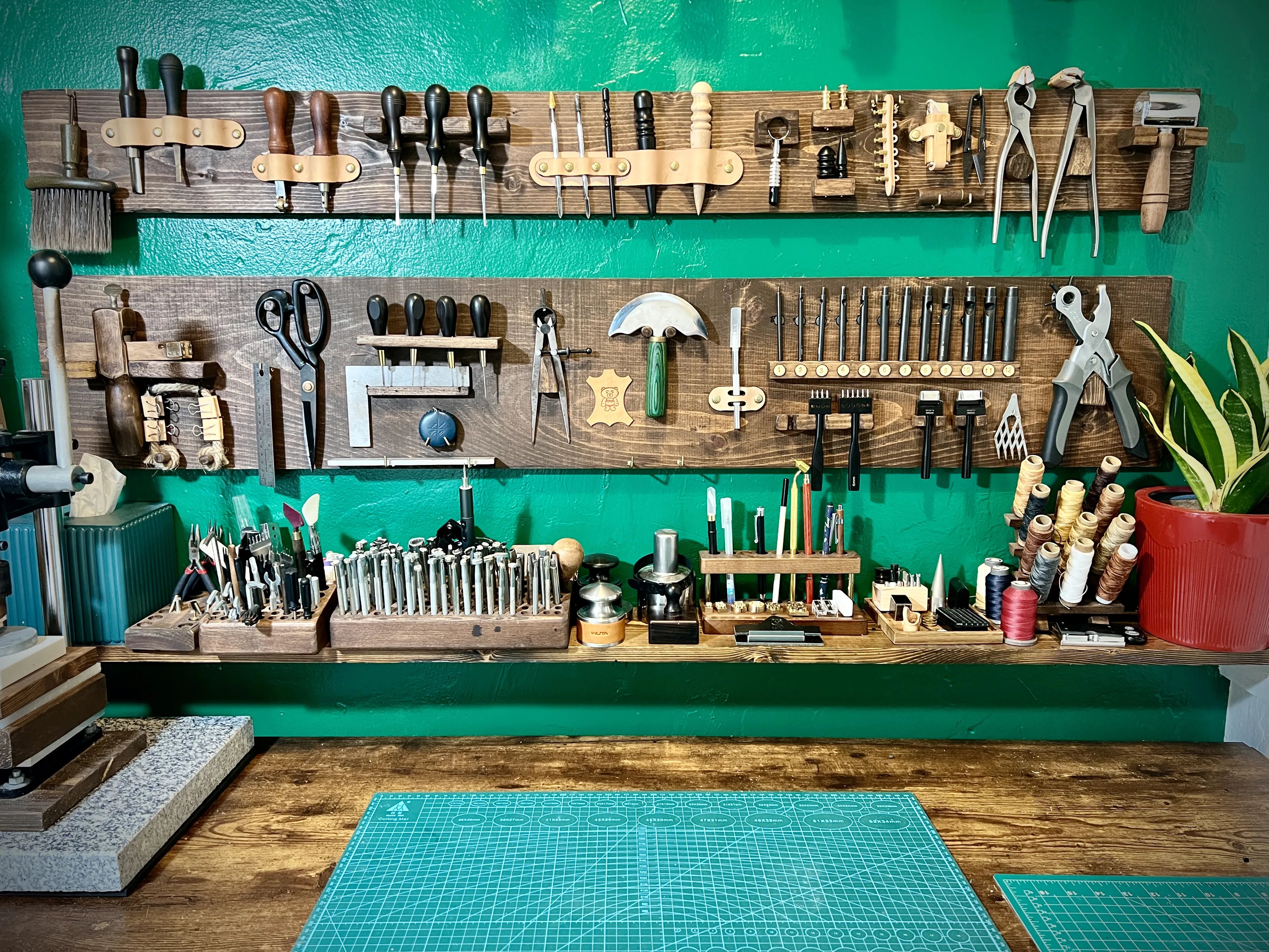 Detailed view of the custom green workshop wall displaying custom dark wood tool racks neatly lined with edge bevelers, punches, scissors, and spools of thread.