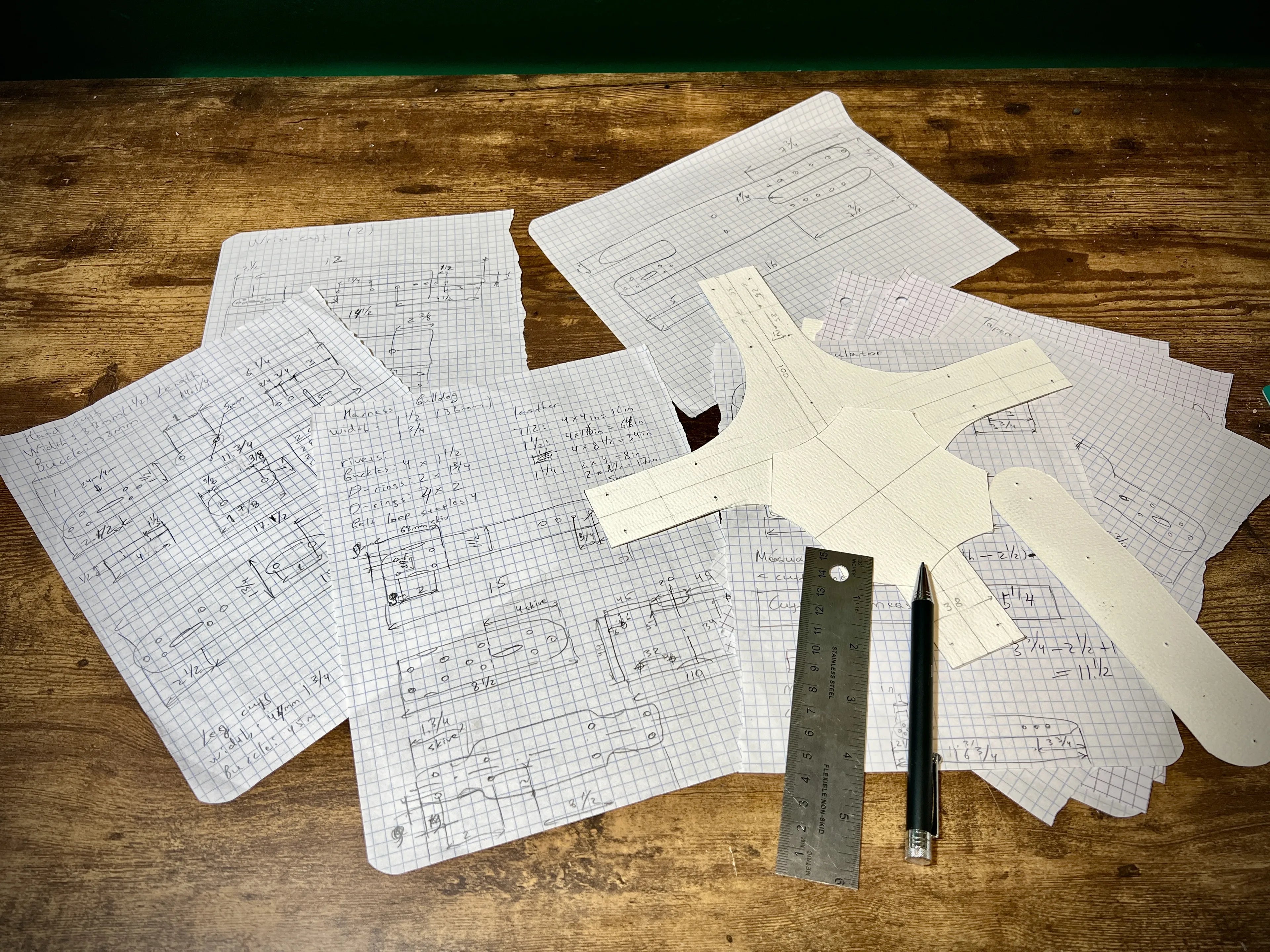 Hand-drawn technical leathercraft pattern schematics and grid design blueprints arranged on a workbench with a stainless steel ruler and a pen.