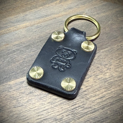 Detail macro view of a Knotty Oso black leather keychain, showcasing the deep debossed bear design and textured starburst brass fasteners.