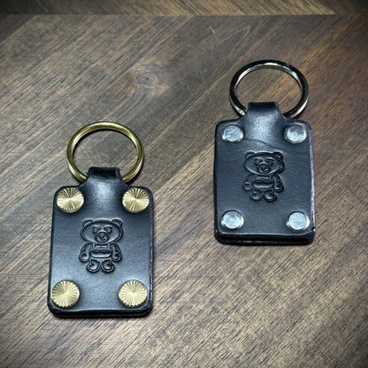 Studio craft view showcasing two black leather keychains side by side to compare the solid brass and nickel-plated steel hardware options.