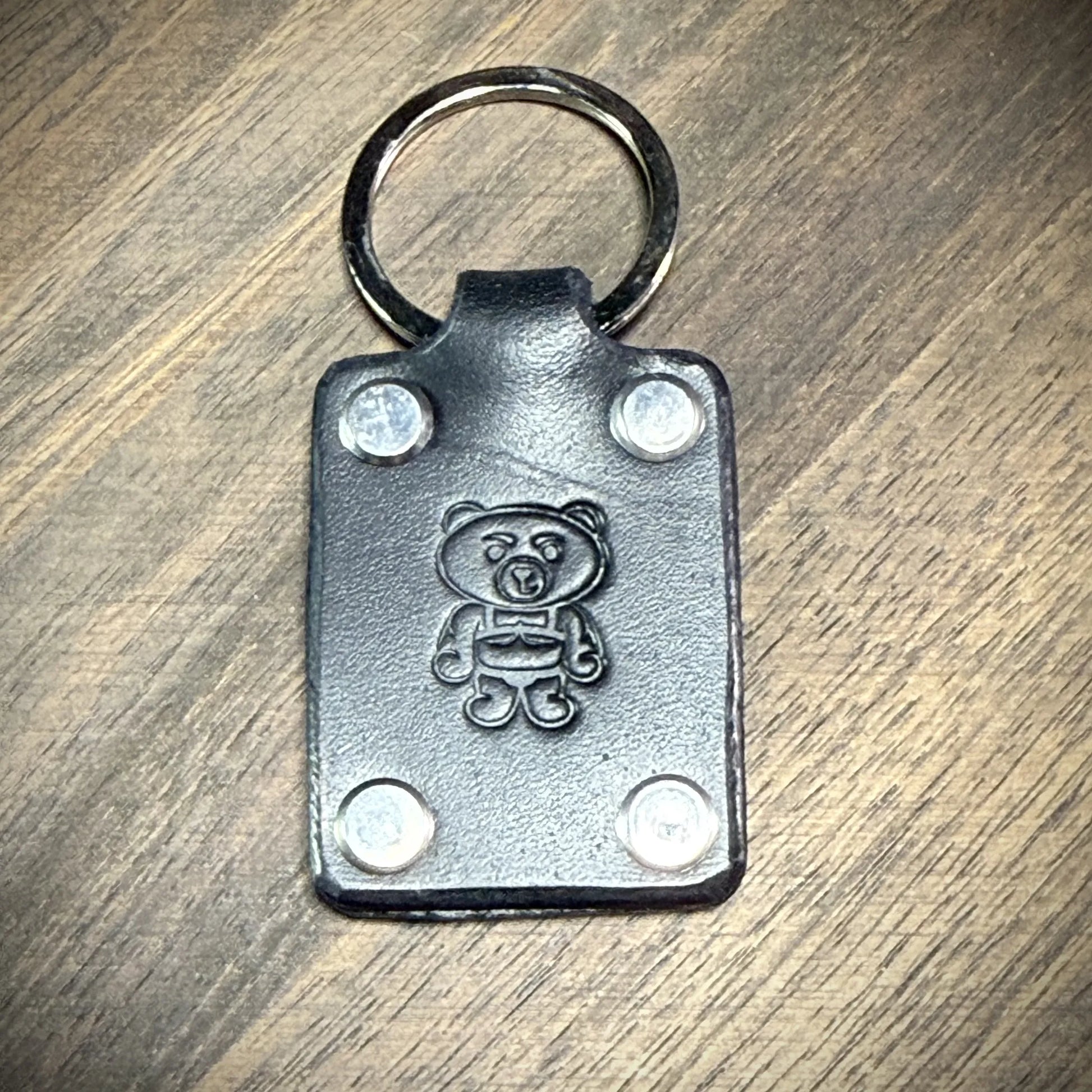 Front-facing view of a black leather keychain assembled with nickel-plated steel hardware, a split ring, and smooth flat-head binding posts.