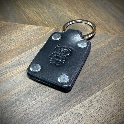 Product reveal view of a black leather keychain highlighting flush-mounted steel fasteners and a heavy-duty steel split ring component.