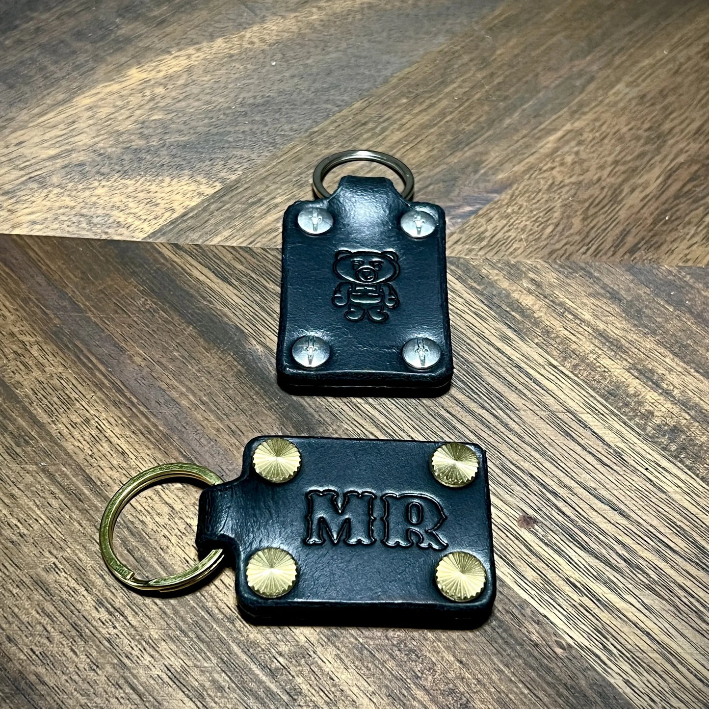 Handcrafted personalized black leather keychains showcasing brass and steel hardware options.