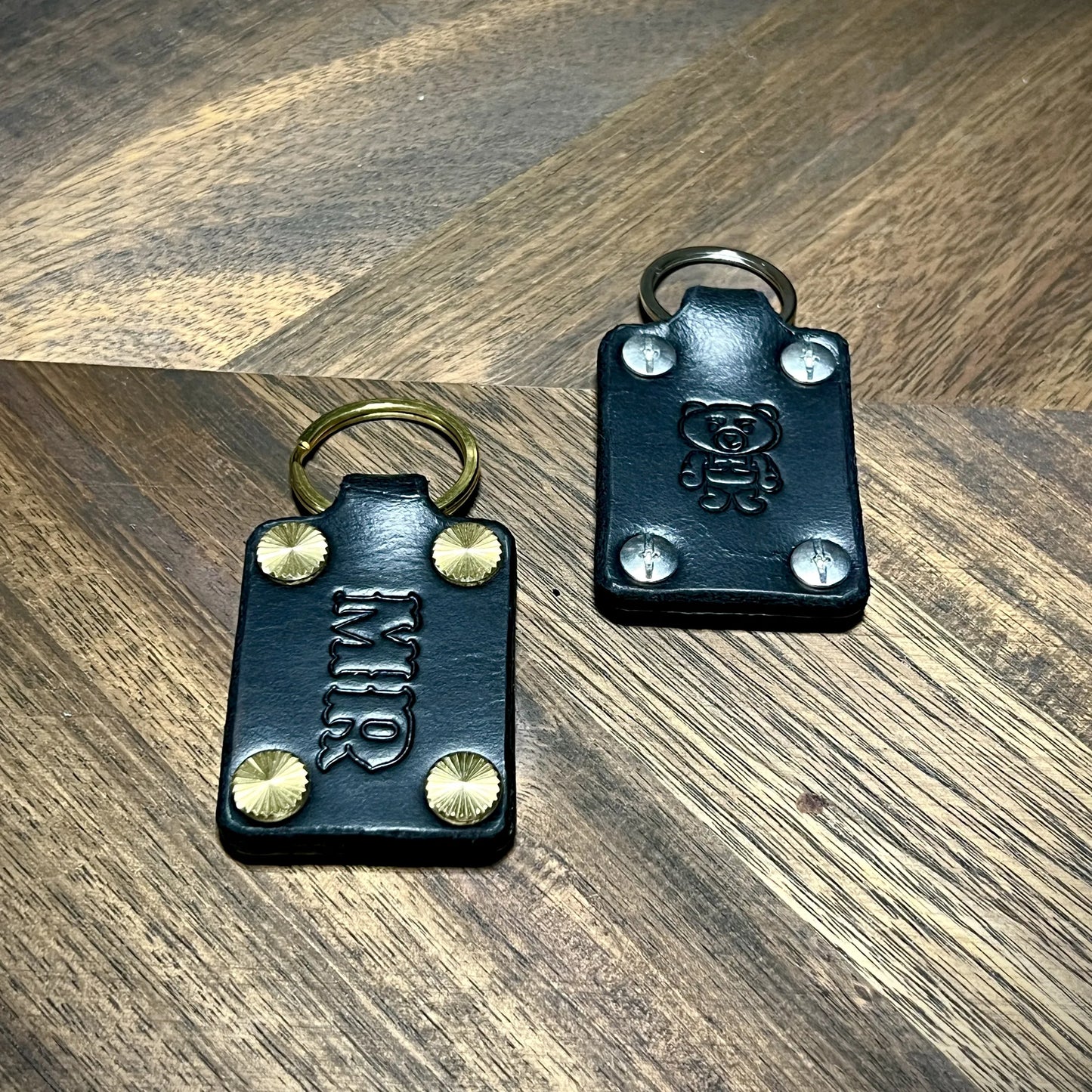 Handmade black leather keychains featuring custom initials and bear stamp with steel and brass hardware.