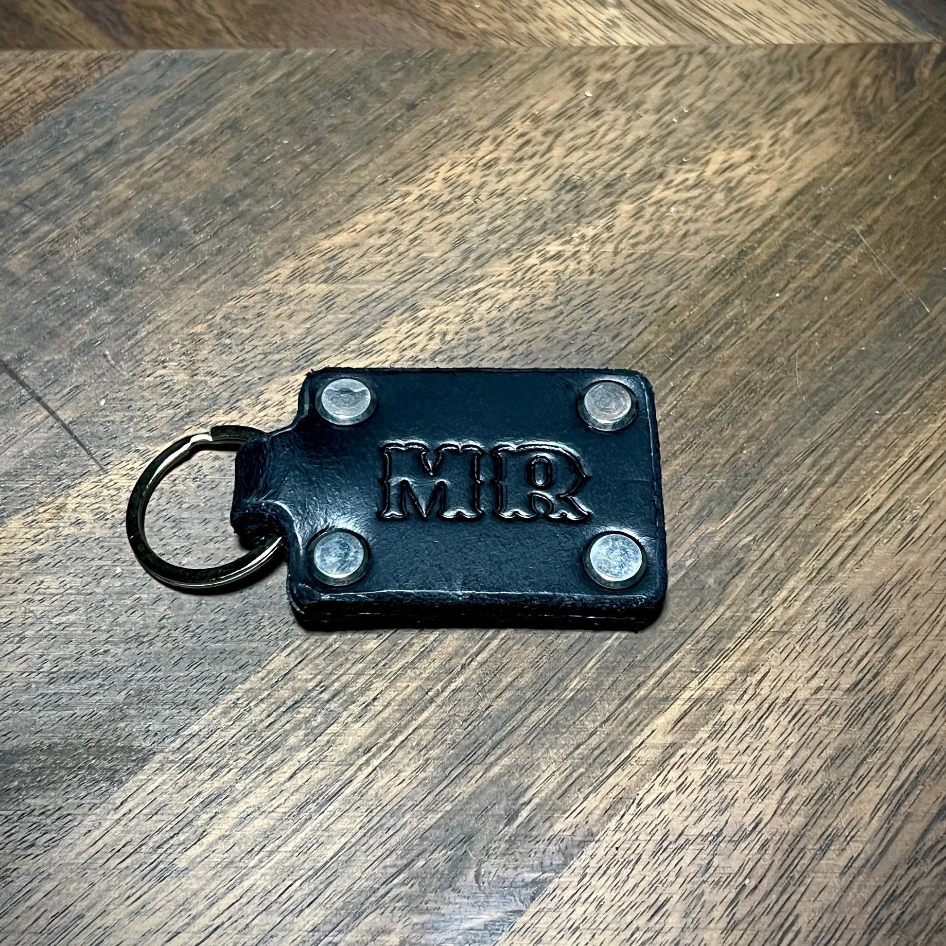 Custom initialed black leather keychain with stainless steel hardware and four corner rivets.