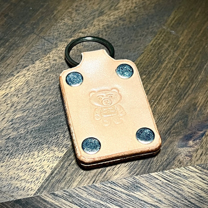 Angled hero view of a natural leather keychain featuring four nickel-plated steel rivets and embossed bear logo.