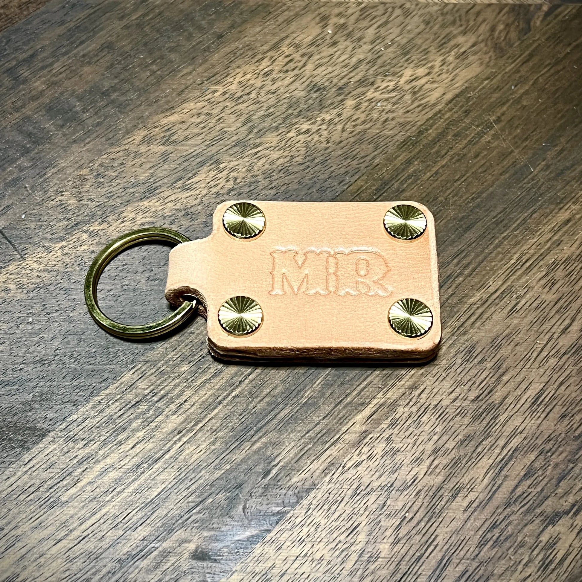 Detail macro of custom MR stamped natural leather keychain held together by four radial sunburst brass screw posts and a brass key ring.