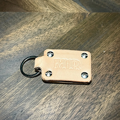 Detail macro of custom MR stamped natural leather keychain secured with four steel Phillips-head screw posts and a steel split key ring.