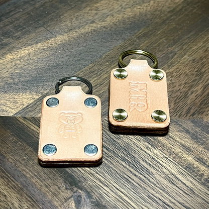 Hero tilt of natural leather keychains featuring embossed bear graphic and custom MIR initials with steel and brass hardware.