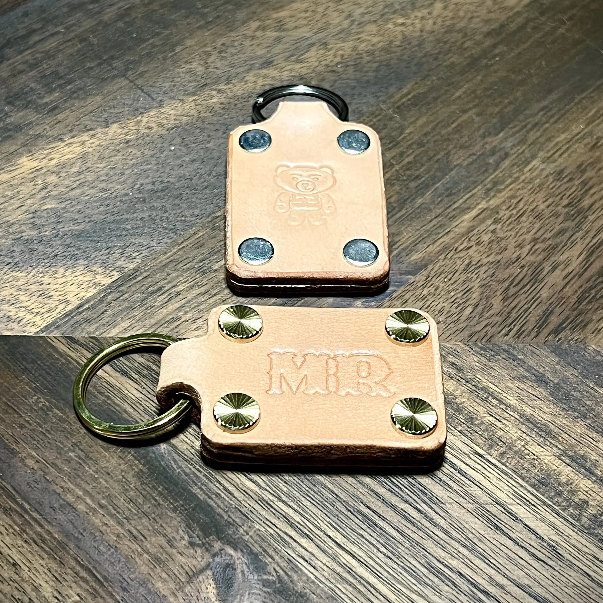 Top-down view of natural vegetable-tanned leather keychains showcasing steel and brass hardware options with embossed details.