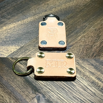 Top-down view of natural vegetable-tanned leather keychains showcasing steel and brass hardware options with embossed details.