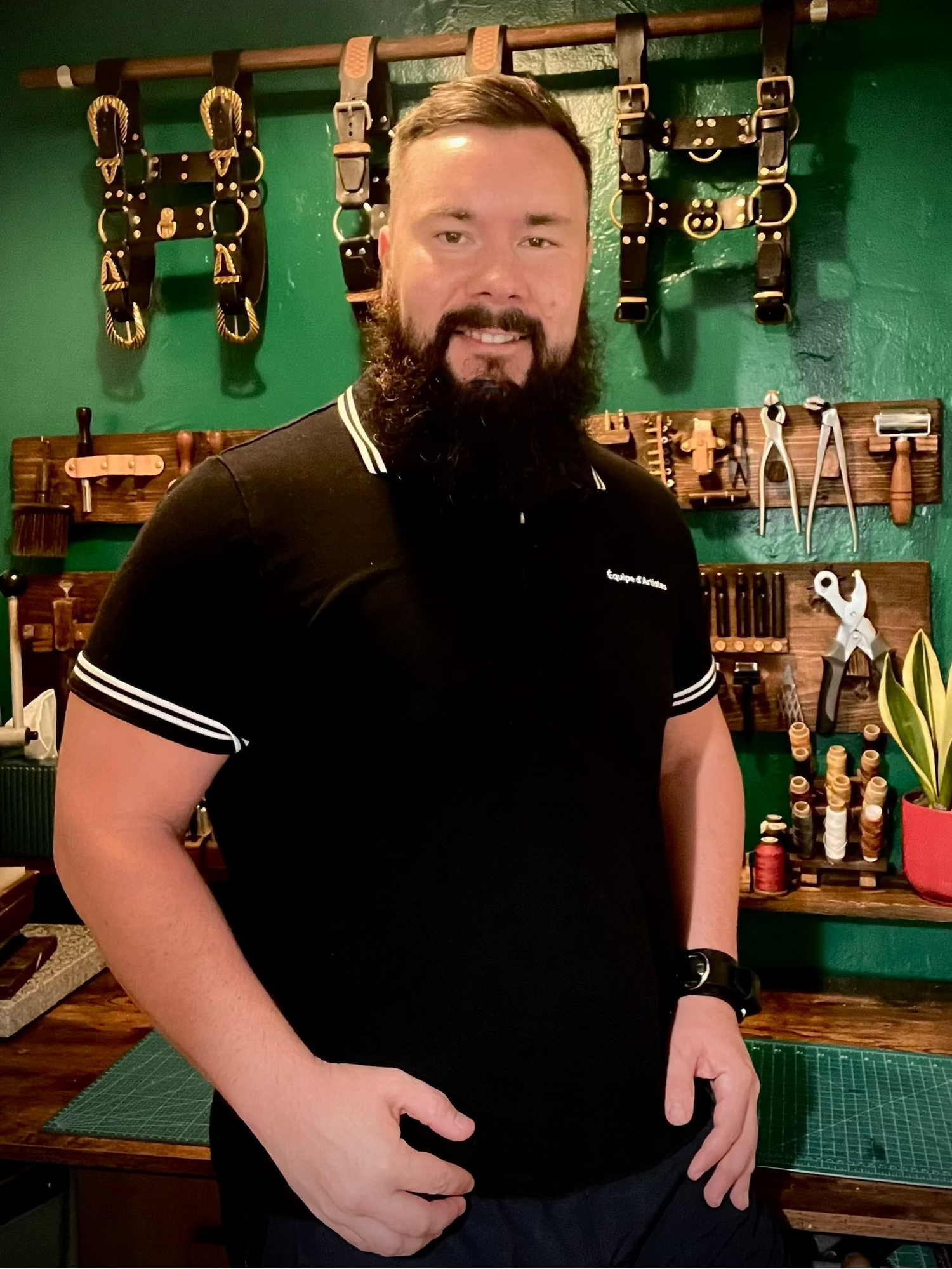 Man with a beard wearing a black polo shirt in a workshop setting