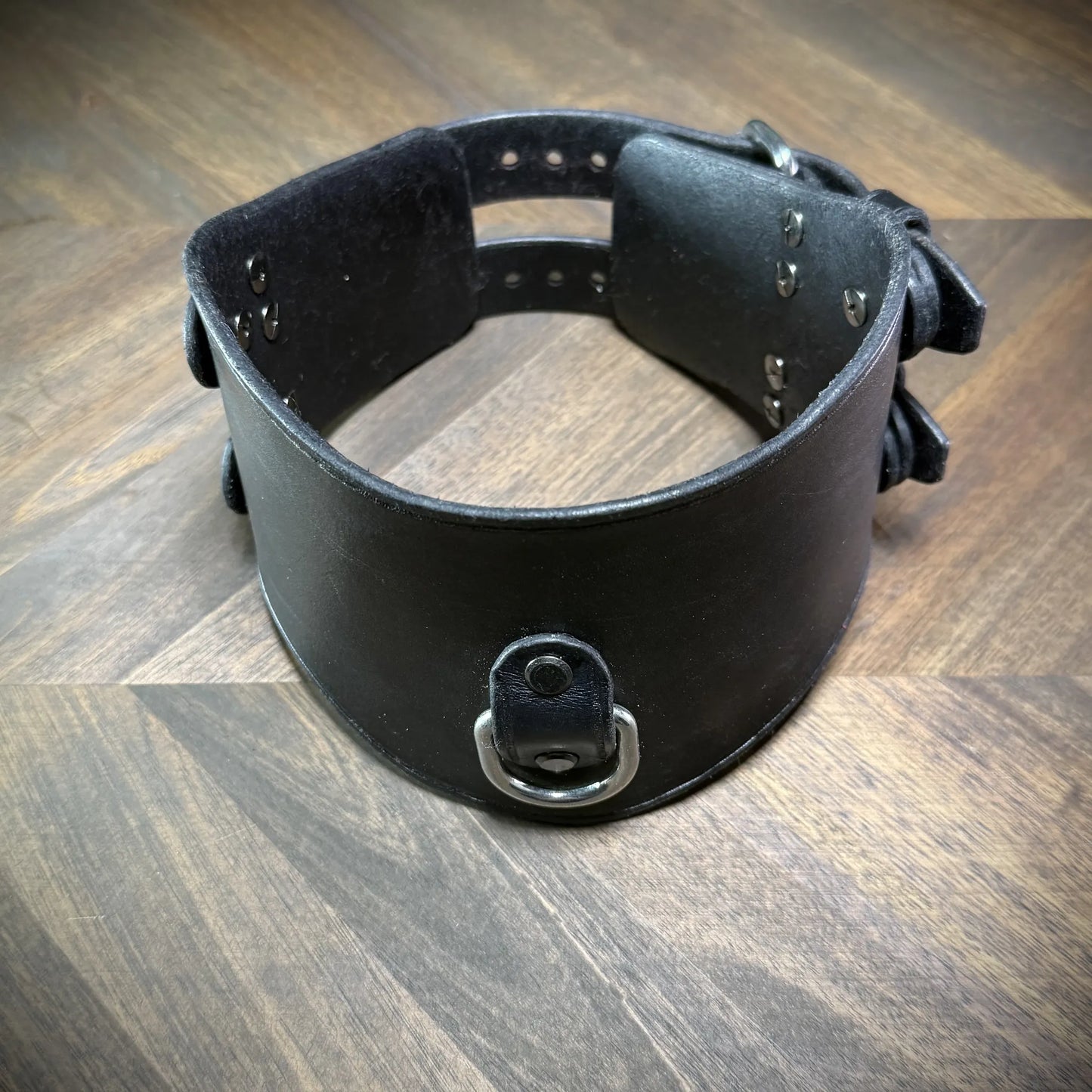 Hero tilt view of a handcrafted black leather posture collar highlighting nickel-plated steel hardware components styled as a subculture accessory.