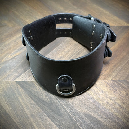 Hero tilt view of a handcrafted black leather posture collar highlighting nickel-plated steel hardware components styled as a subculture accessory.