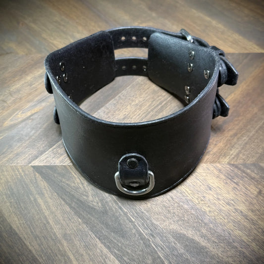 Hero tilt view of a handcrafted black leather posture collar highlighting nickel-plated steel hardware components styled as a subculture accessory.