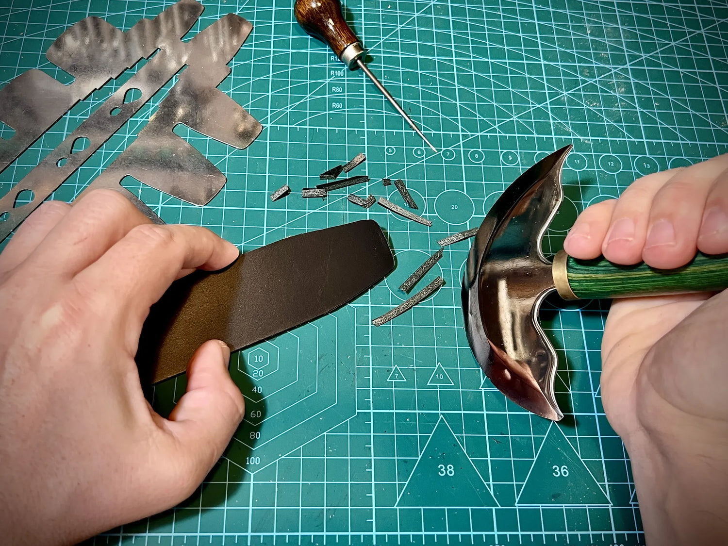 Artisan using a green-handled head knife to slice a premium black leather strap end on a grid cutting mat.