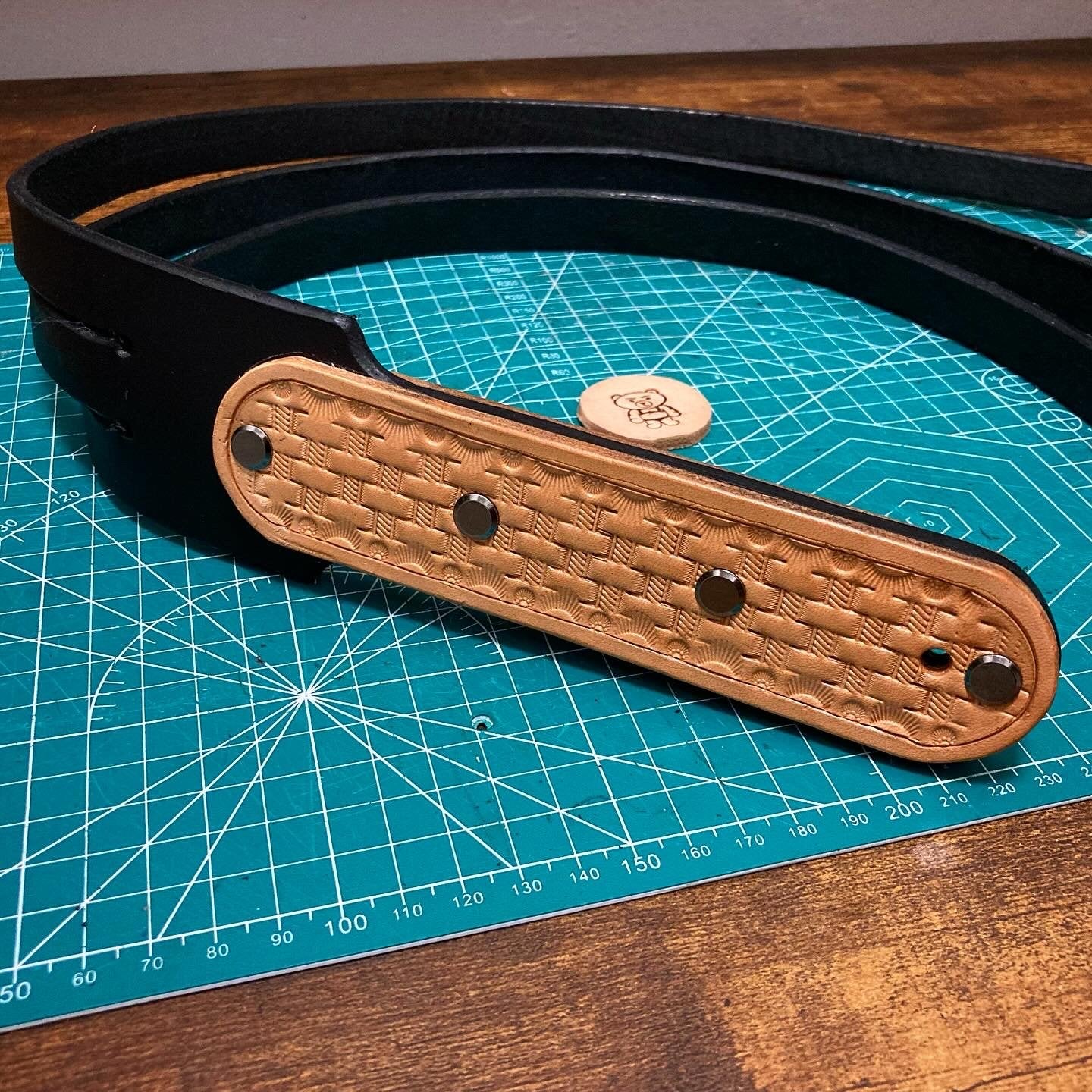 Handcrafted black leather strap with a natural basketweave overlay secured with steel rivets on a cutting mat.