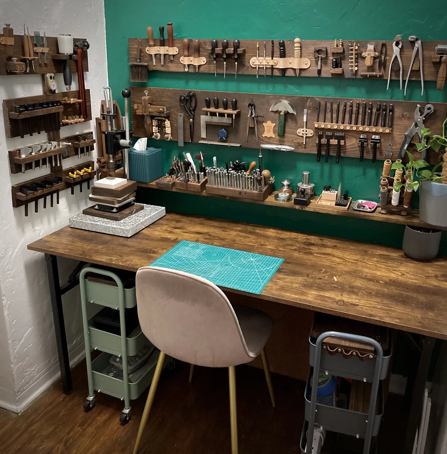 Overview of the leathercraft workshop workbench displaying hand tools, clicker press, and a green grid cutting mat.