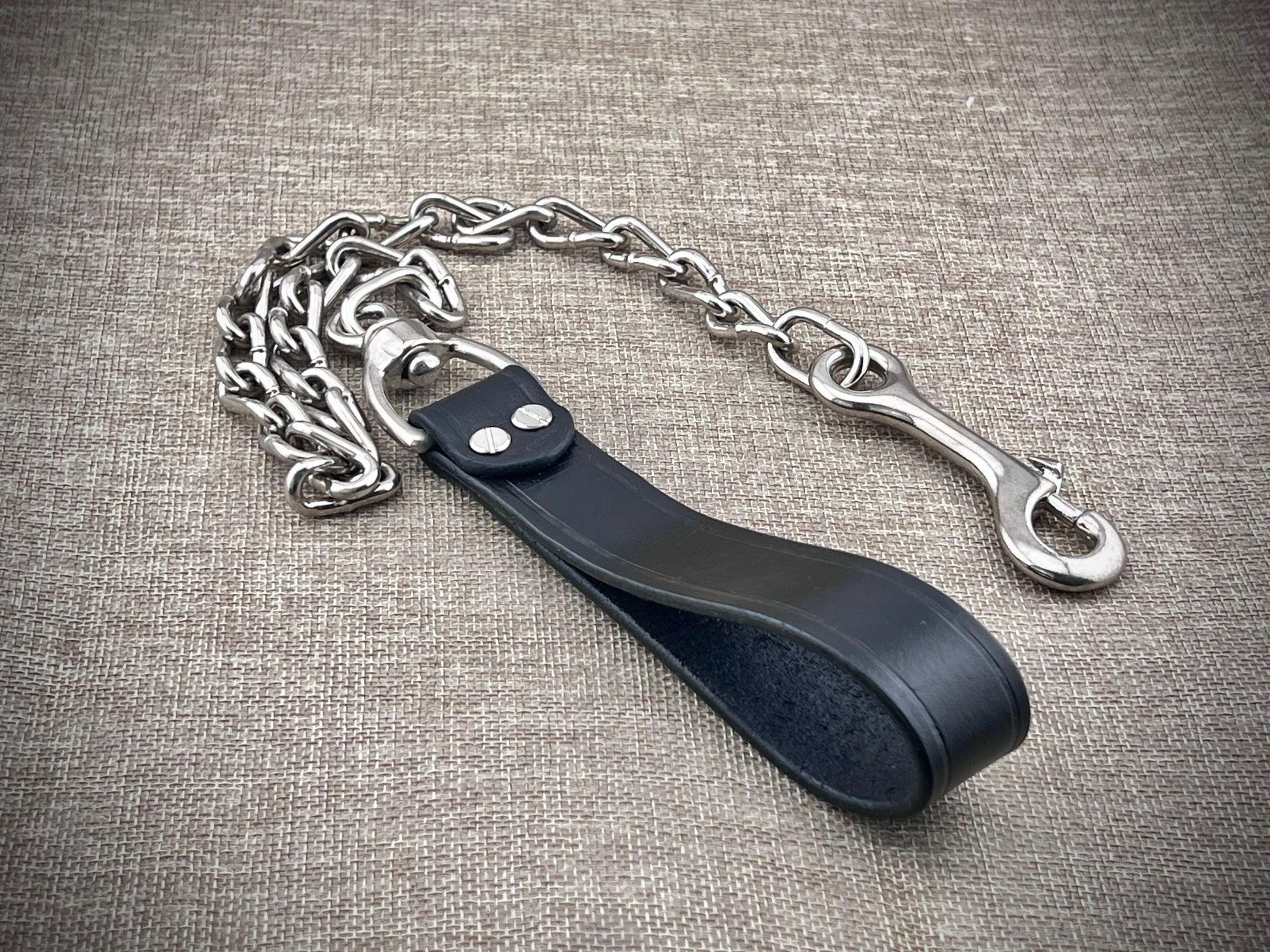 Metal chain with a black leather strap on a textured gray background