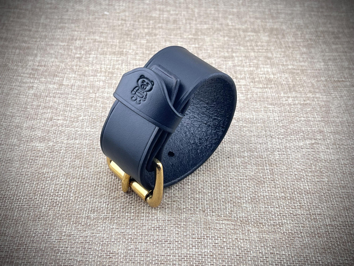 black leather bracelet with gold buckle on a textured gray background