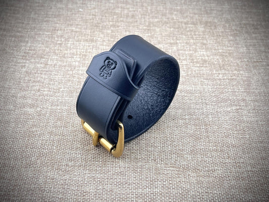 black leather bracelet with gold buckle on a textured gray background