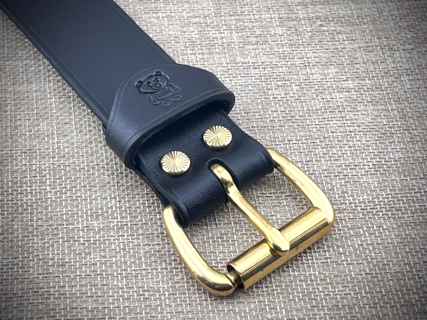Black leather bracelet with gold buckle on a textured gray background