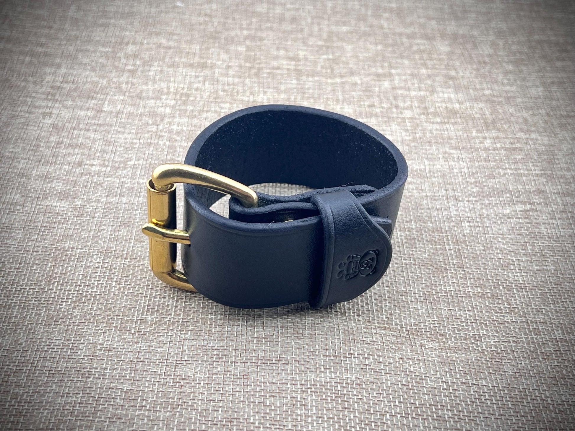 Black leather strap with a brass buckle on a textured gray background