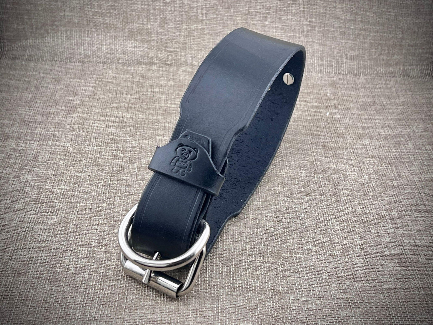Black leather collar with steel buckle on a textured gray background