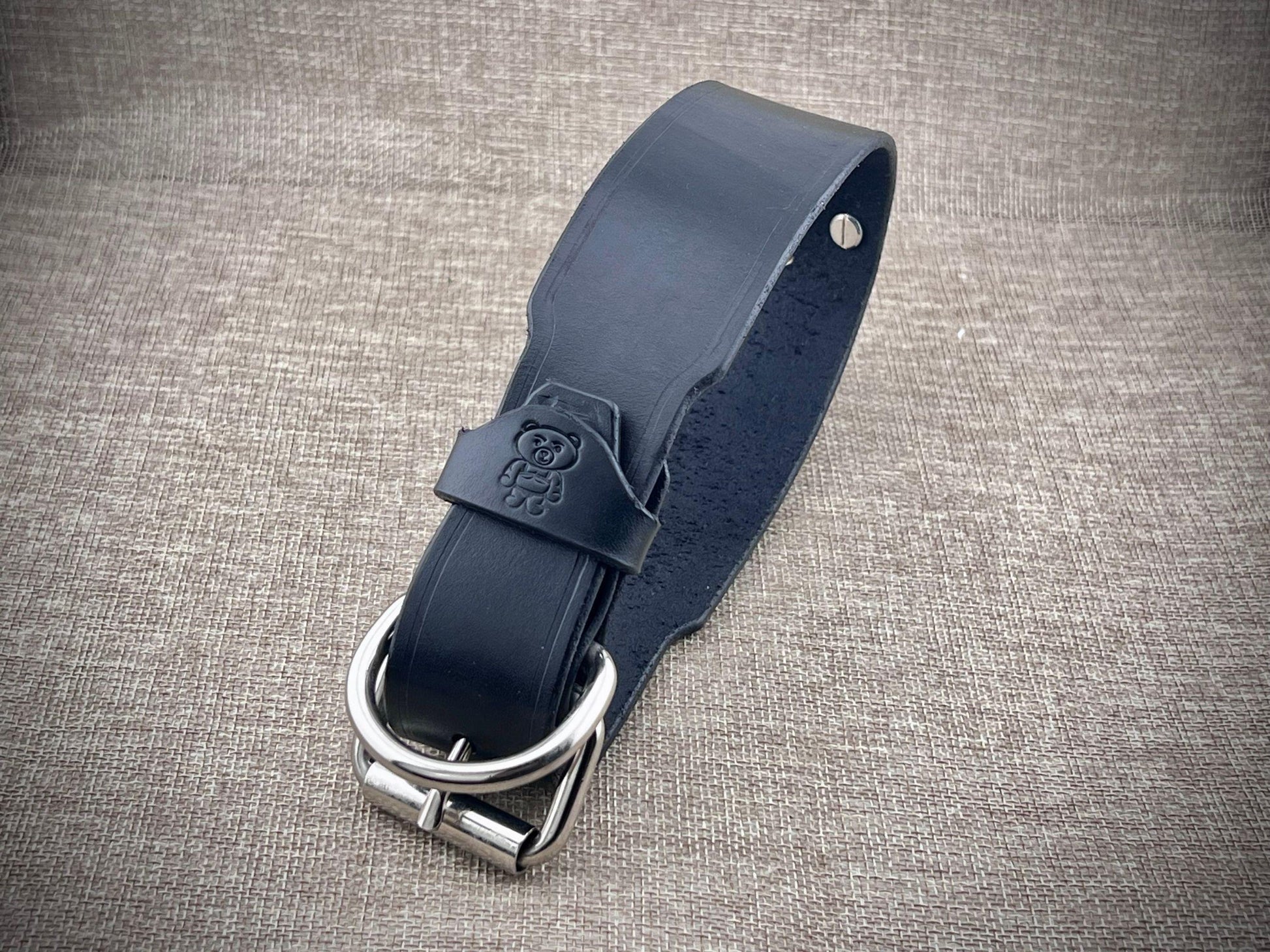 Black leather collar with steel buckle on a textured gray background