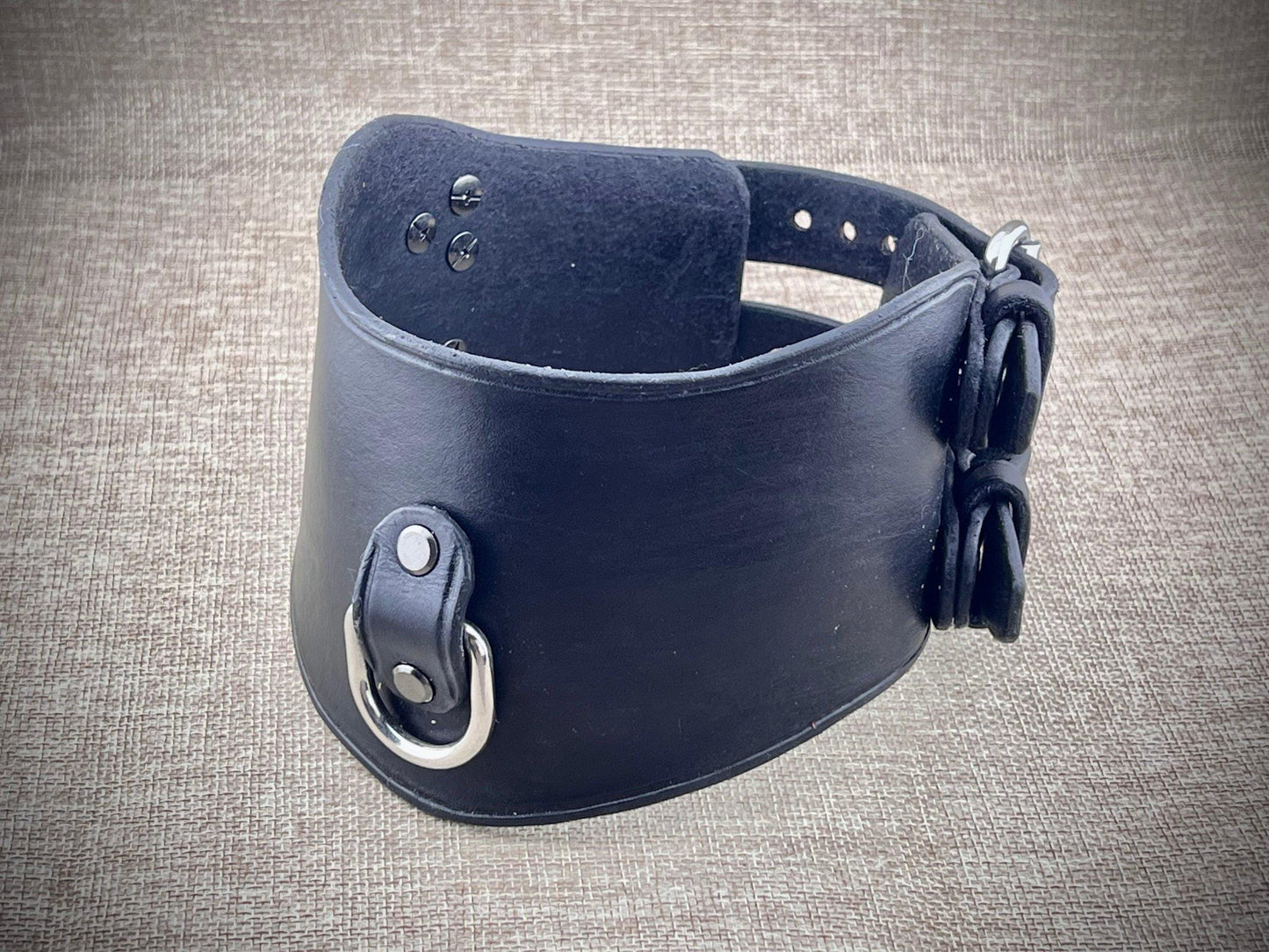 Black leather collar with metal hardware on a textured gray background