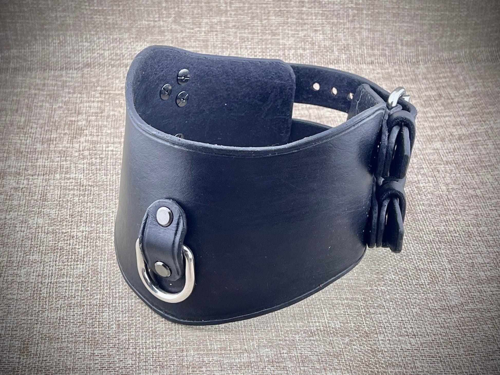 Black leather collar with metal hardware on a textured gray background