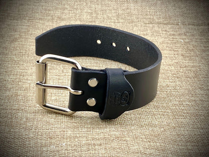 Black leather belt with silver buckle on a textured beige background