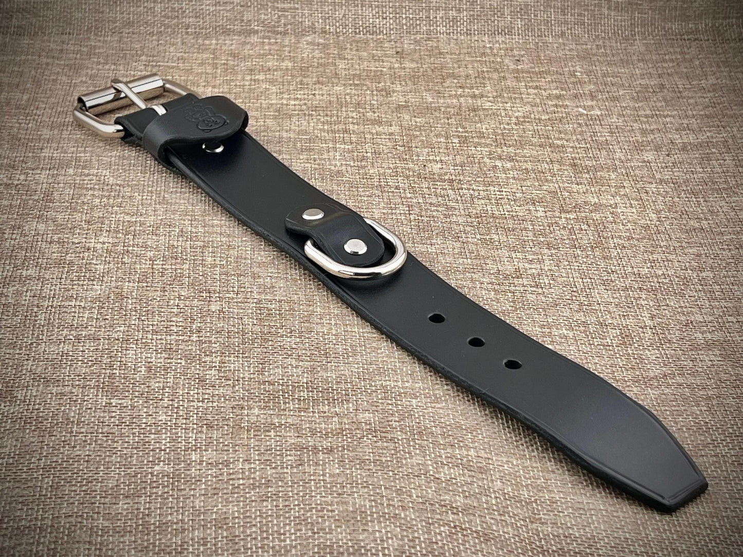 Black leather belt with silver buckle on a textured brown background
