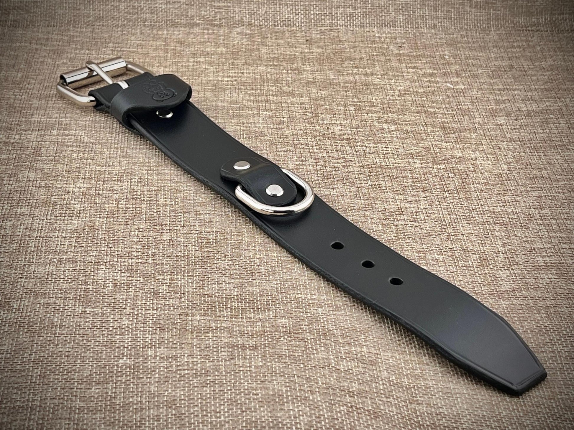 Black leather belt with silver buckle on a textured brown background