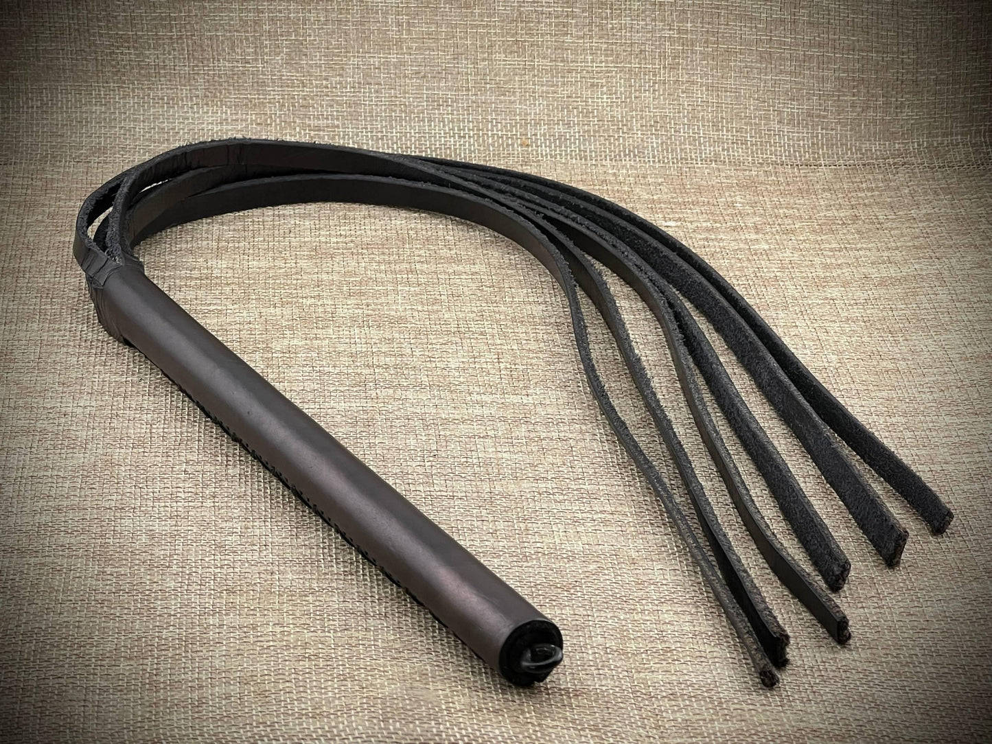 Black leather flogger on a textured beige background