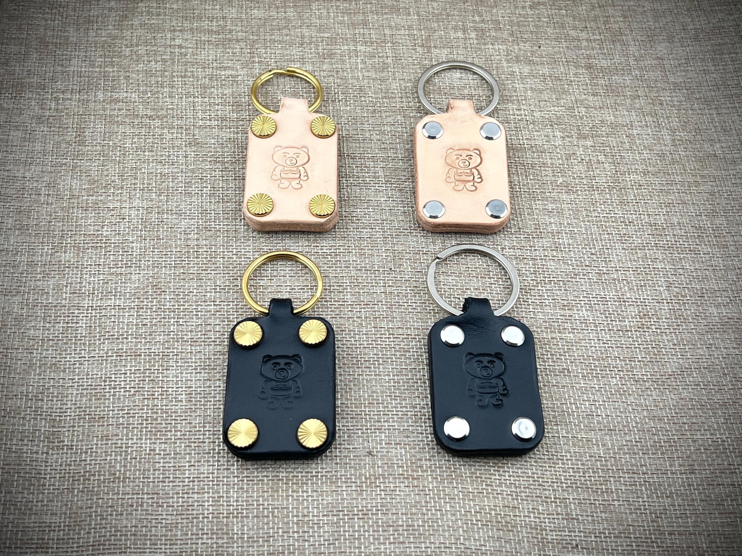 Four leather keychains with metal loops on a textured gray surface