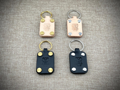 Four leather keychains with metal loops on a textured gray surface