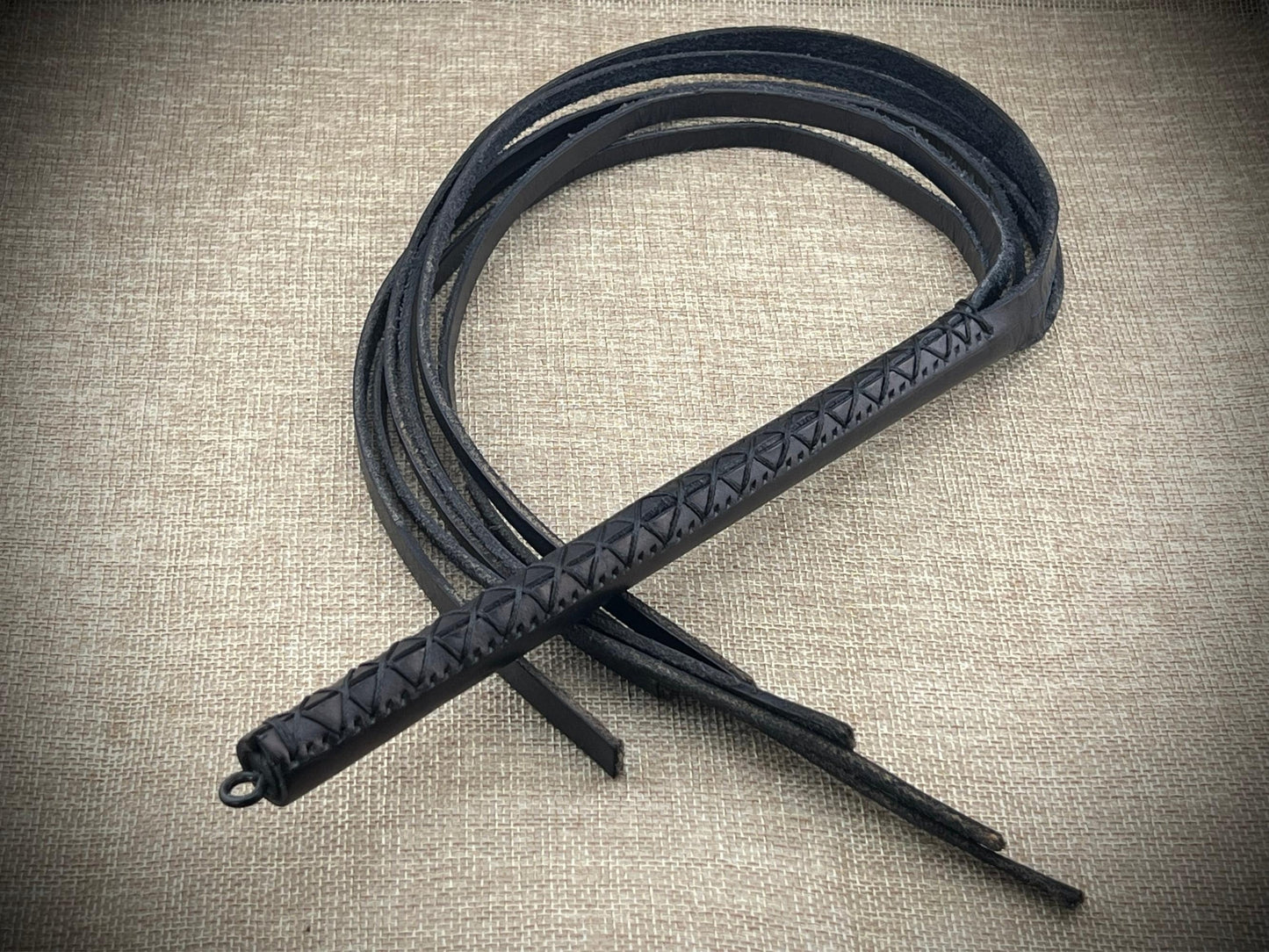 Black leather whip with intricate patterns on a textured beige background