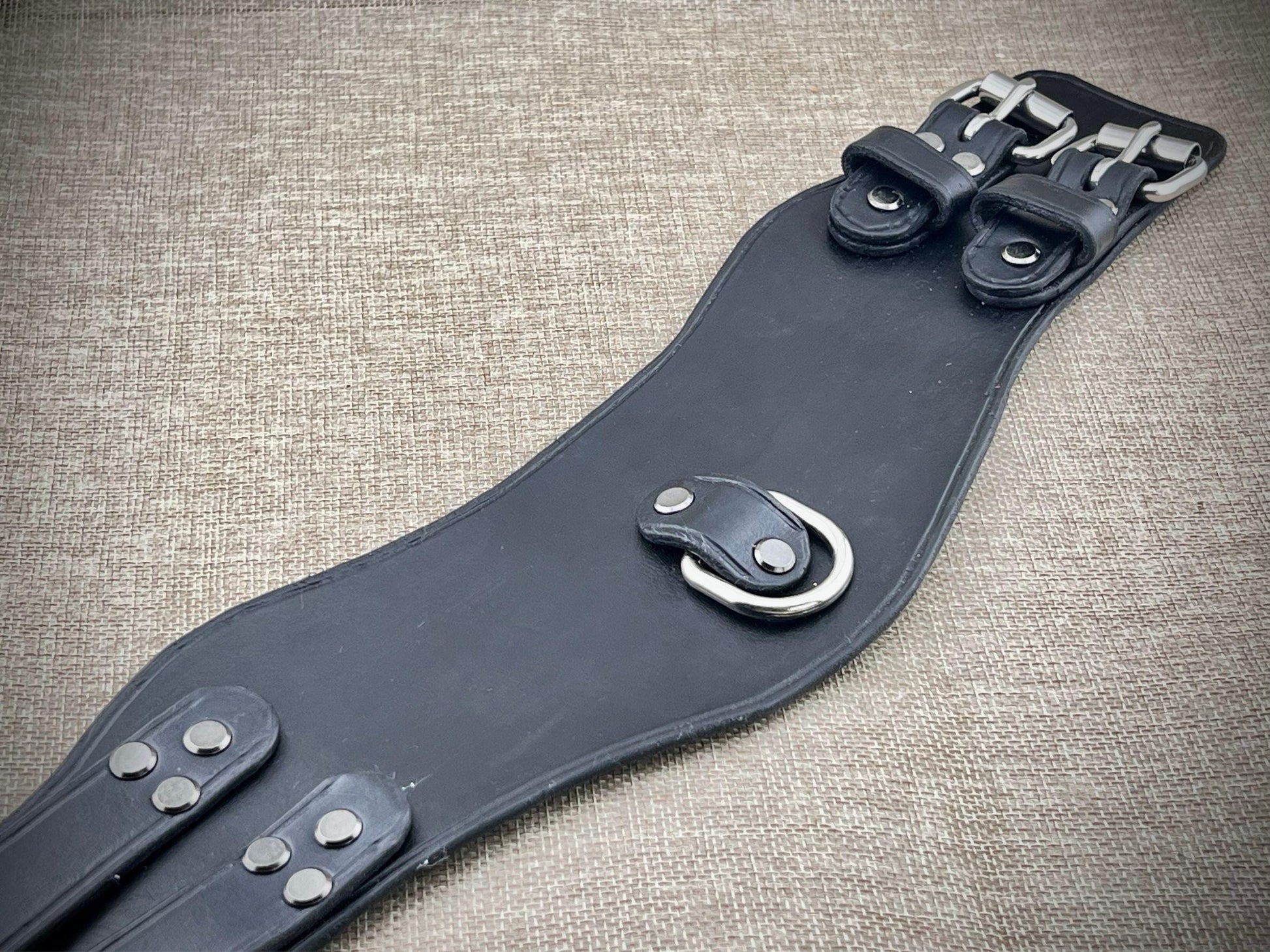 Black leather collar with metal hardware on a textured fabric background