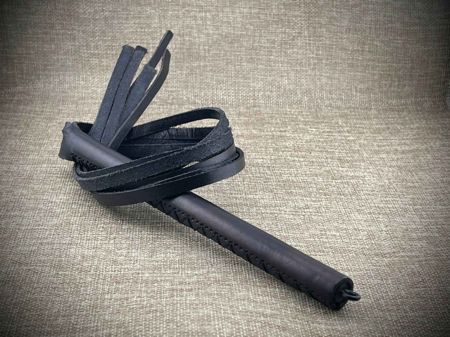 Black leather whip on a textured beige background