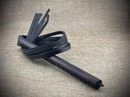 Black leather whip on a textured beige background