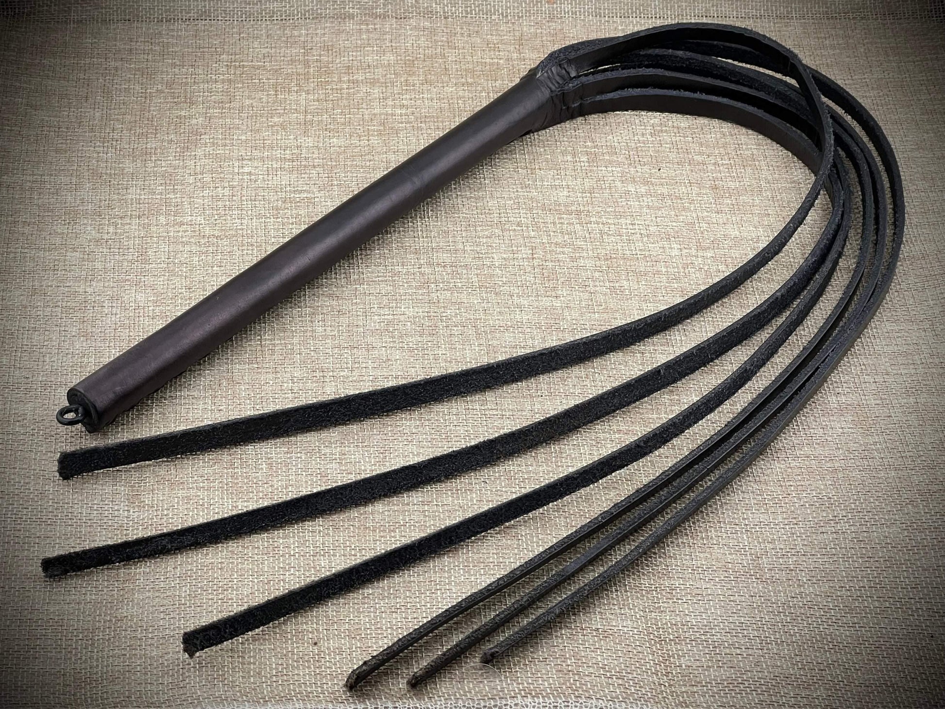 Black leather whip on a textured beige background