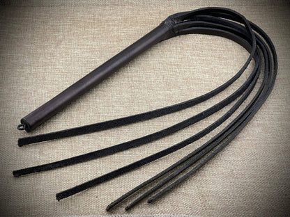 Black leather whip on a textured beige background