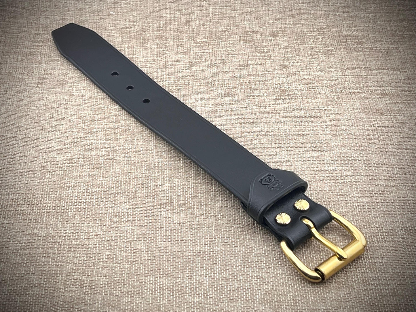 Black leather strap with brass buckle on a textured beige background